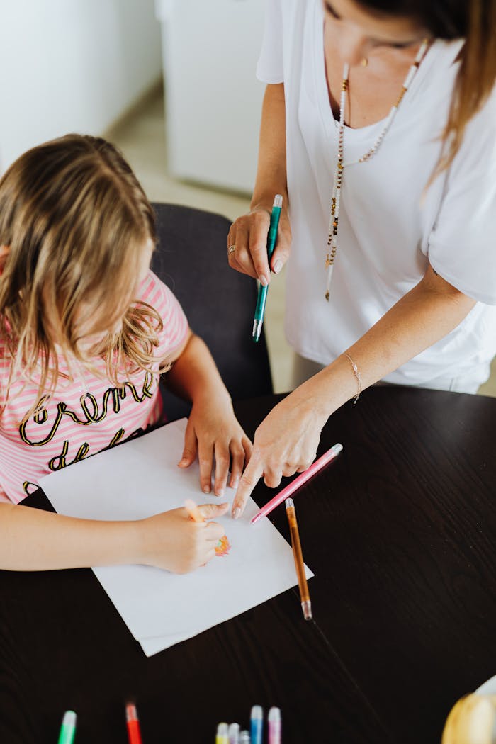 A woman guides her daughter in drawing with colored pens on paper at home.